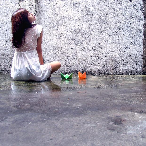 Girl sitting on floor next to two paper boats
