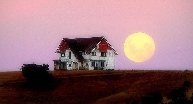 House in field in front of big moon