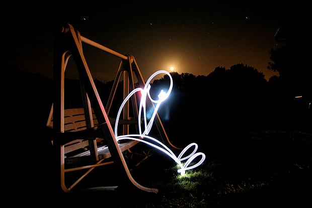 Man made from light sitting on swing