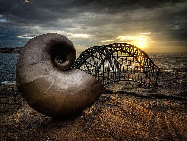 Shell and bridge sculpture by the sea at sunset