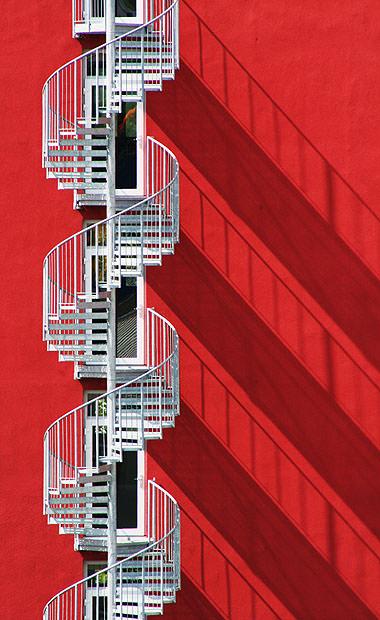 Spiral stairs against a red wall with long shadows